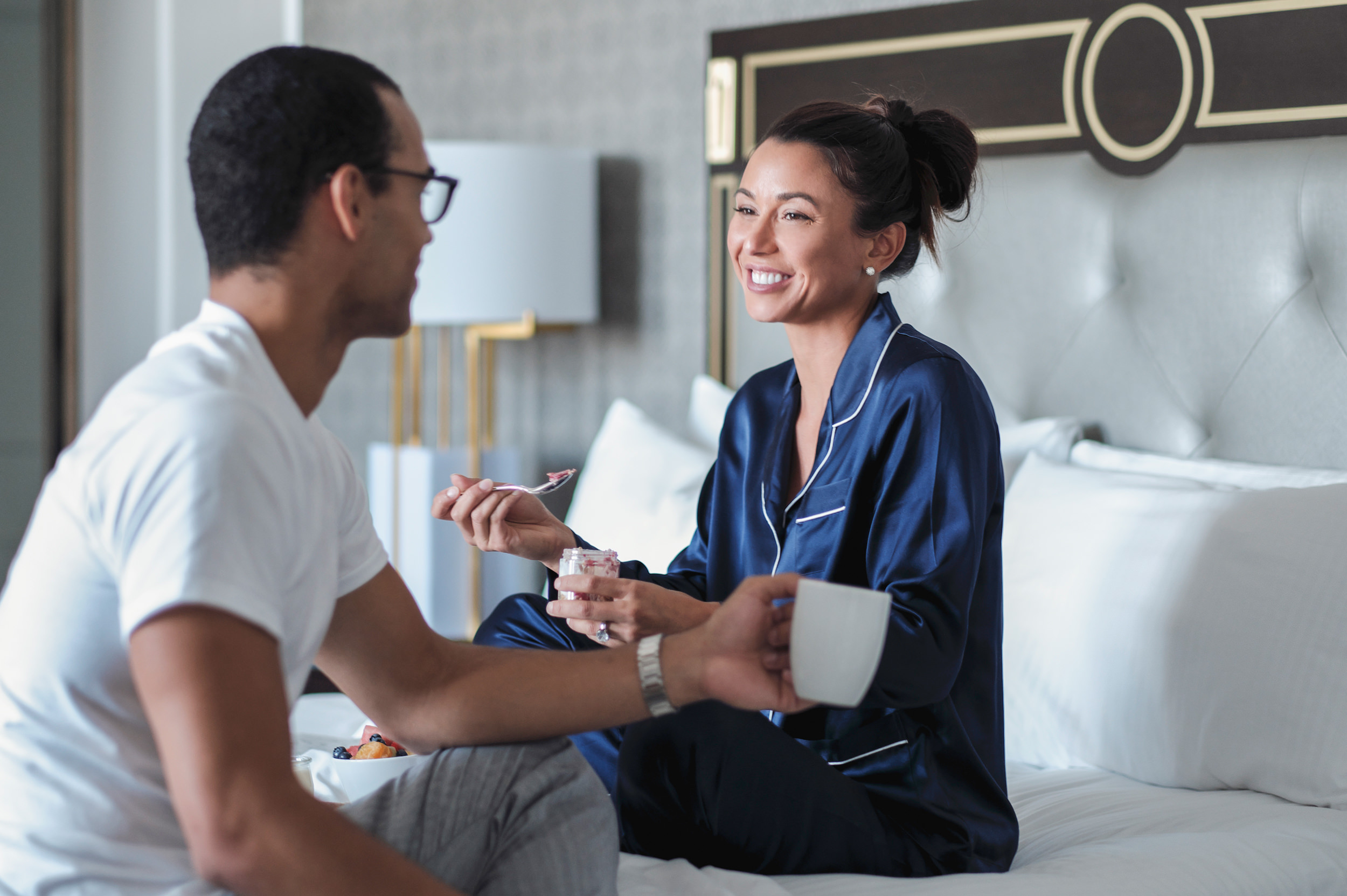 a couple sit on a bed eating breakfast