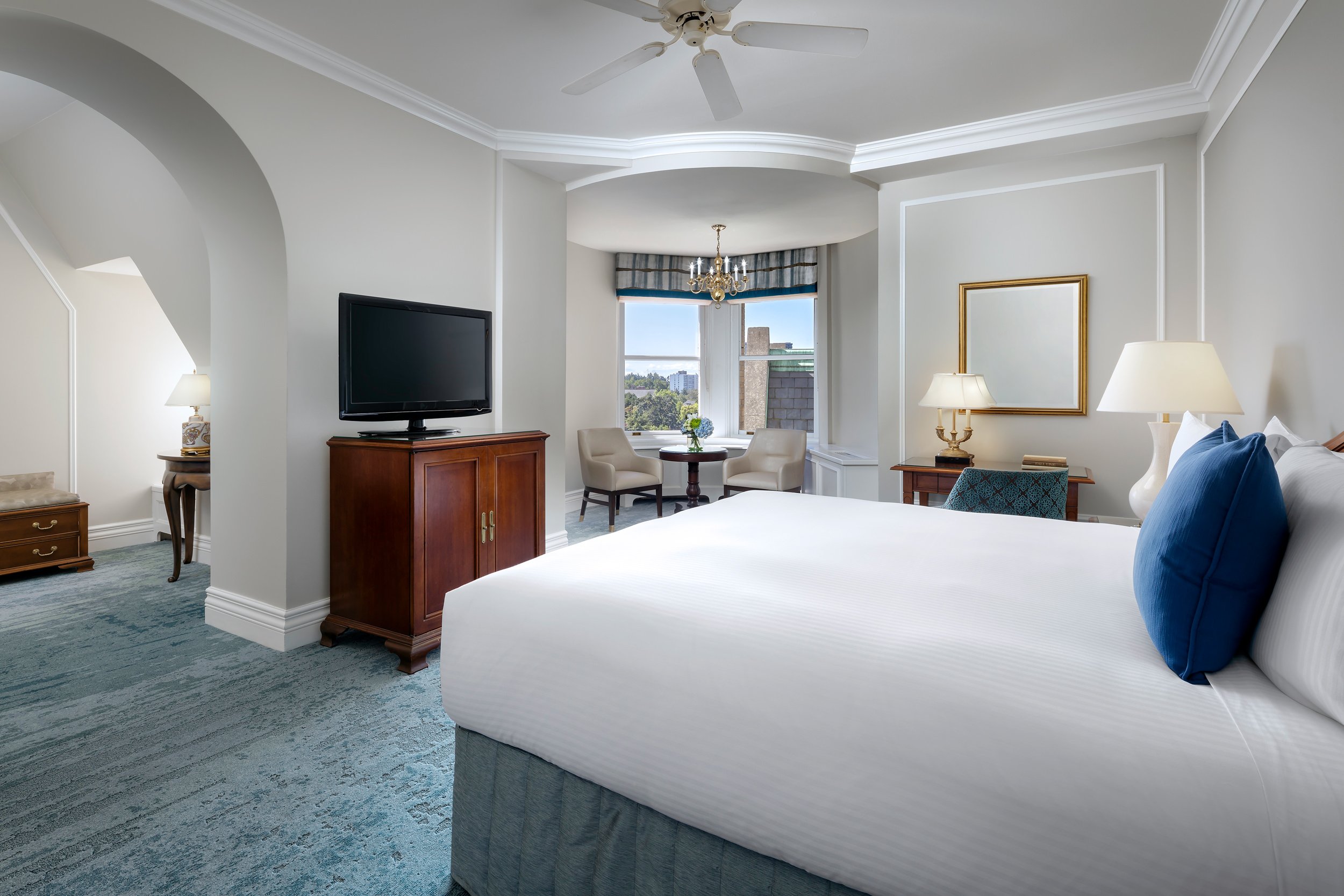 white bedroom with a television, and two lounge chairs in front of a window