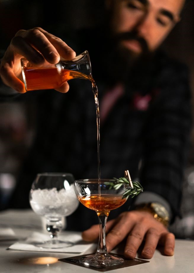 man pouring a shot into a cocktail